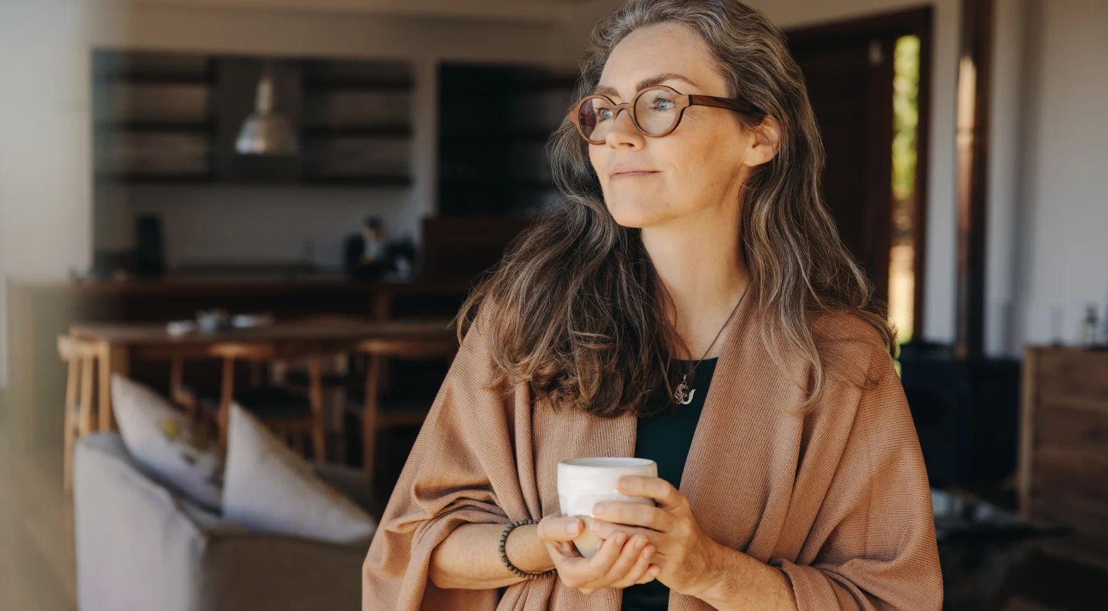 Donna che guarda altrove pensierosa mentre è in piedi con una tazza di tè