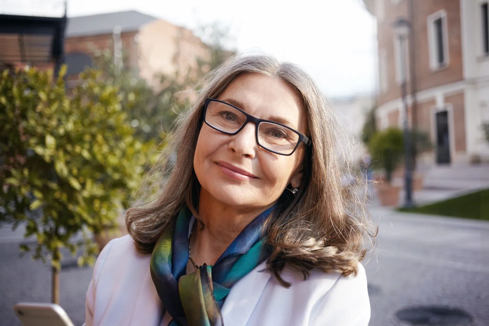 Woman with glasses in street with trees and buildings
